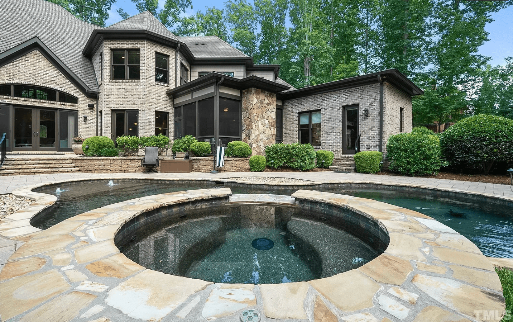 A stunning gray brick home with a deep teal swimming pool with spa and green landscaping